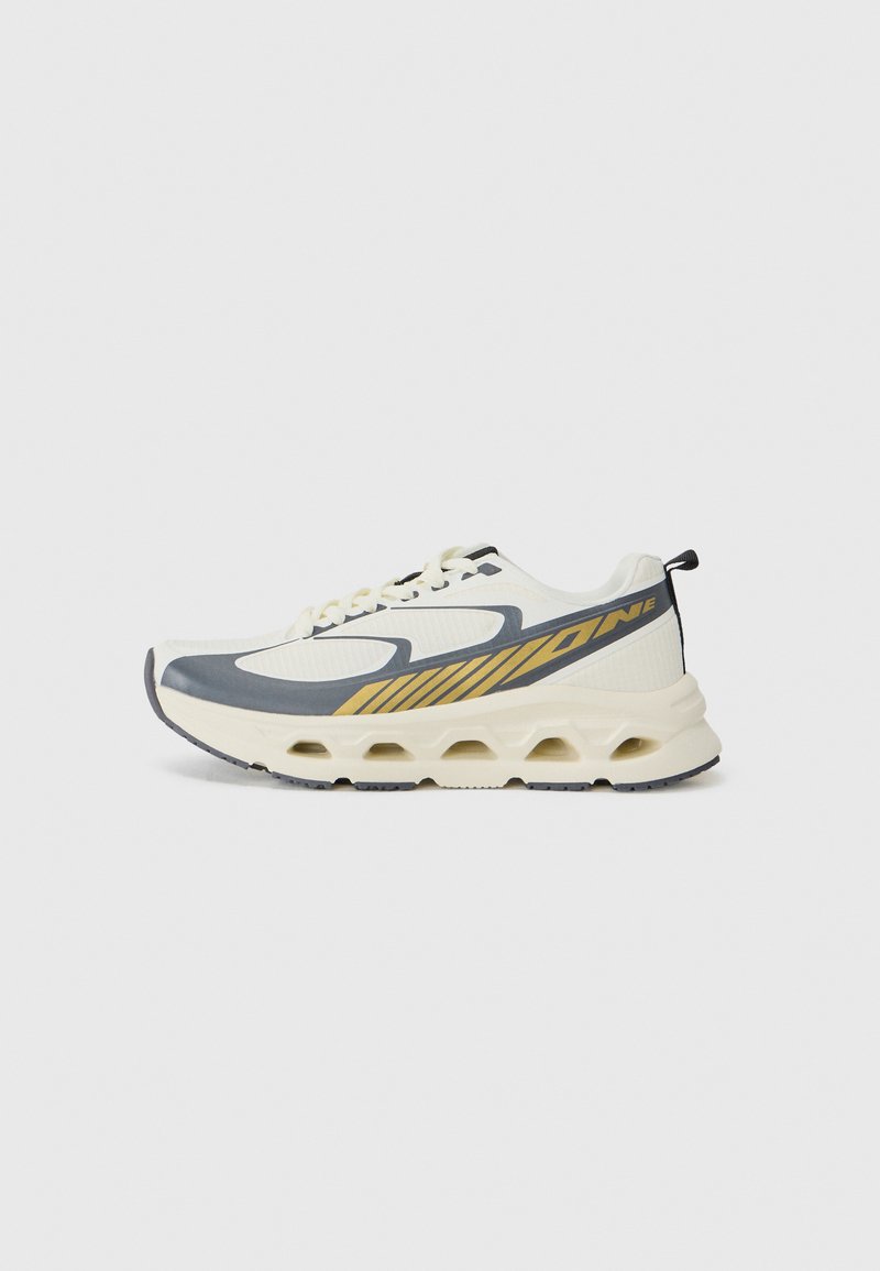 White athletic shoe with gray accents, a textured design, and yellow stripes. Features a thick sole with cutouts for cushioning and support.