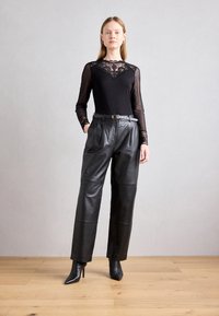 Blouse noire à manches longues avec détail en dentelle au niveau du col, associée à un pantalon en cuir noir taille haute et des talons aiguilles noirs.