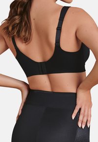 Zwarte sportbh met brede banden en verstelbare sluitingen. Heeft een gladde textuur en een scoop rugontwerp voor comfort en ondersteuning.