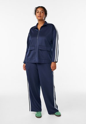 Námornícky modrý teplákový komplet s bielymi bočnými pruhmi, zipsová bunda s dvoma prednými vreckami a zodpovedajúce nohavice. Textúrovaná látka a voľný strih.