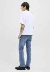 Camiseta blanca de manga corta combinada con jeans de color azul claro. Los jeans presentan un sutil detalle de costura en los bolsillos traseros. Unos zapatos negros completan el look.