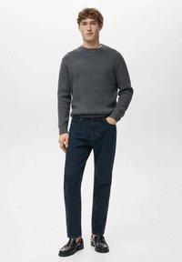 Suéter gris acanalado, vaqueros azul oscuro y zapatos de cuero negro. Diseño simple con escote redondo y silueta de pierna recta.