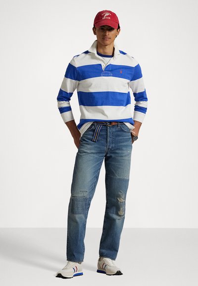 Polo shirt cu mânecă lungă, cu dungi albe și albastre, asortat cu blugi deteriorați albaștri și adidași albi cu accente roșii și albastre. Cămașă roșie.