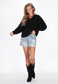 Fekete kötött pulóver V nyakkal, összeillő világoskék szakadt denim rövidnadrággal és fekete velúr bokacsizmával. Színes nyaklánc kiemelés.