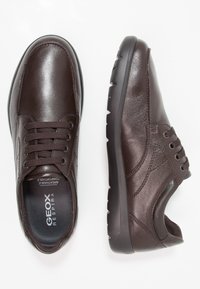 Een paar donkerbruine leren veterschoenen voor casual gebruik, één bovenaanzicht dat de binnenzool toont en één zijaanzicht dat de zwarte rubberen zool laat zien.