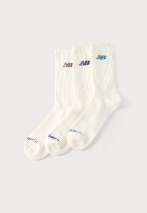 Drie paar witte sokken met boordjes en ribstructuur, elk met een "NB" logo in een andere kleur vlak bij de bovenkant en bijpassende tekst op de tenen.