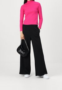 Obepnutý rolák ve světlé růžové barvě, spárovaný s černými kalhotami s širokými nohavicemi. Modelka má malou černou kabelku se stříbrným nápisem a bílé tenisky.