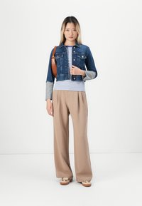 Denim jacket with a cropped design, light blue material, and button closure. Paired with a striped long-sleeve top and beige wide-leg pants.