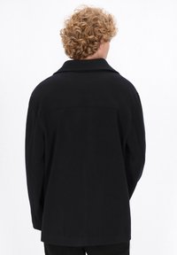 Abrigo de lana negro con un corte holgado, gran cuello y mangas largas. Textura suave con un diseño minimalista, que presenta una costura central en la parte posterior.