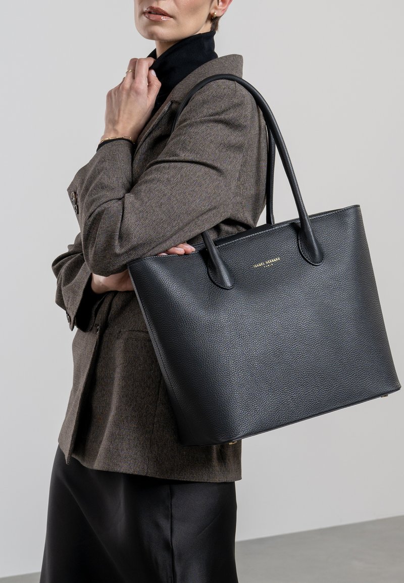 Sac fourre-tout en cuir noir avec finition texturée, doté de deux poignées robustes et d'un design minimaliste. Accent en logo doré à l'avant.