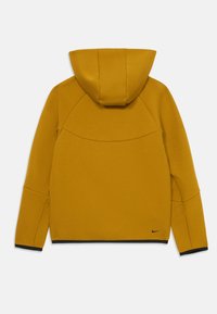Žuta dukserica s kapuljačom od glatkog materijala. Ima zaobljenu kapuljaču, raglan rukave i crni rub na donjem dijelu. Nike logo u crnoj boji.