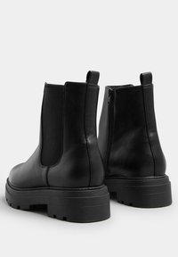 Svarta läder Chelsea-stövlar har en slät yta, elastiska sidopaneler, en bakre dragflik och en kraftig, mönstrad sula.