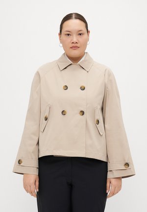 Beige kort jakke med dobbelspent knapper, skrå lommer og vide ermer. Laget av glatt, lett stoff.