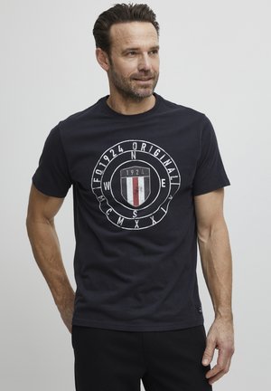 Navy blue cotton t-shirt with a circular logo design featuring the text "1924 Original" and a striped shield in red and white. Short sleeves.