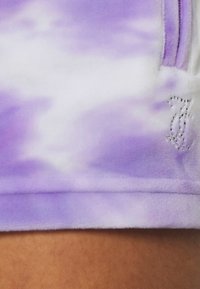 Purple tie-dye fleece shorts with a soft texture, featuring a rhinestone-accented logo on the hem.