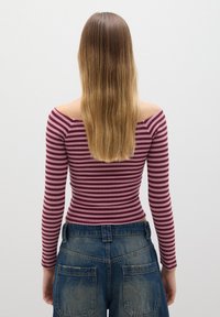 Langärmliges Oberteil in burgunderrot und rosa Streifen, Off-Shoulder-Design, kombiniert mit hochgeschnittenen blauen Jeansshorts mit großen Gesäßtaschen.