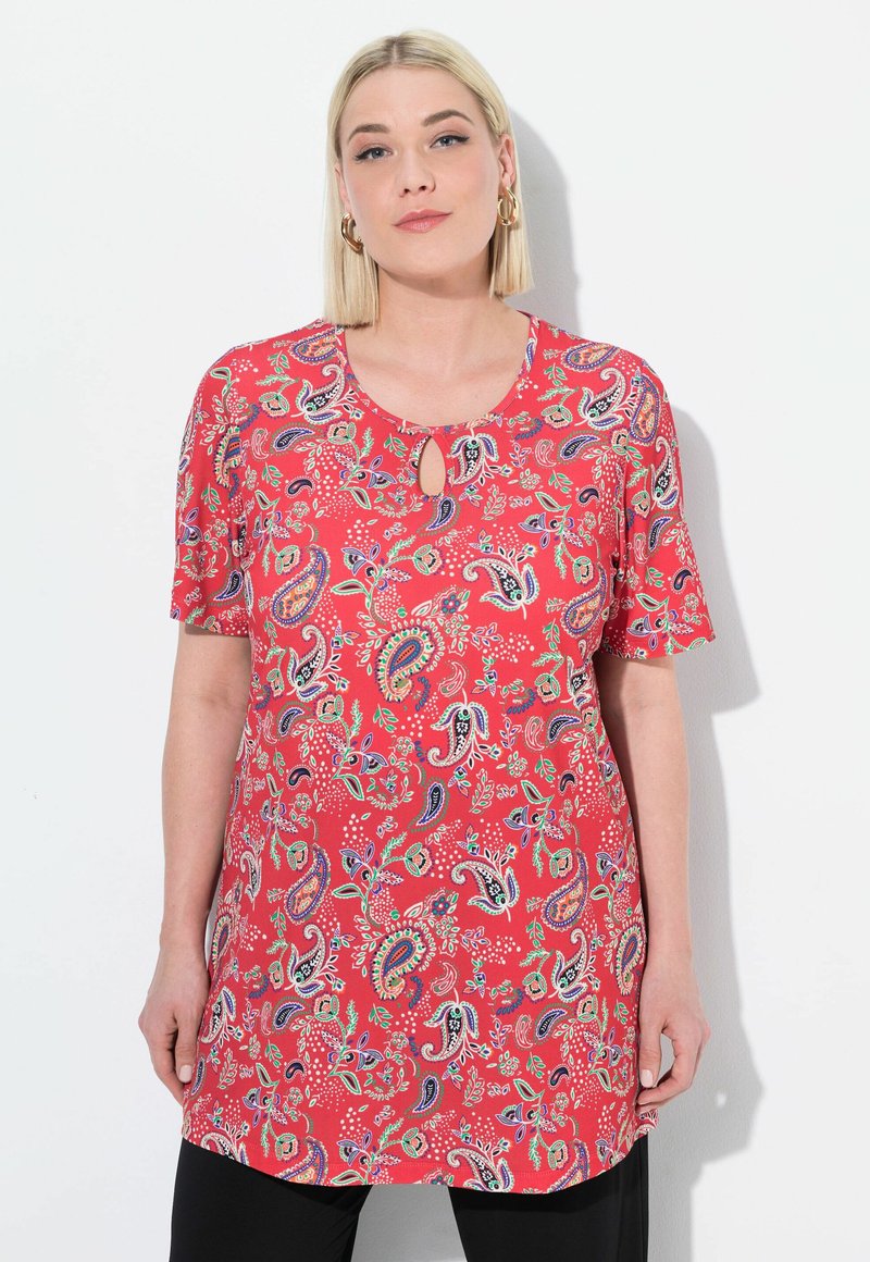 Červená tunika s paisley vzorem, krátkými rukávy a detaily v oblasti krku ve tvaru klíčové dírky. Obsahuje barevné květinové a paisley vzory po celé ploše.
