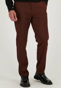Pantalons marron avec une texture lisse, coupe ajustée et poches avant, associé à des chaussures noires brillantes, créant un look formel.