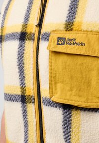 Gilet in pile con un motivo a quadri giallo e blu navy, dotato di una tasca in tessuto gialla e una zip nera. Etichetta del marchio visibile sulla tasca.
