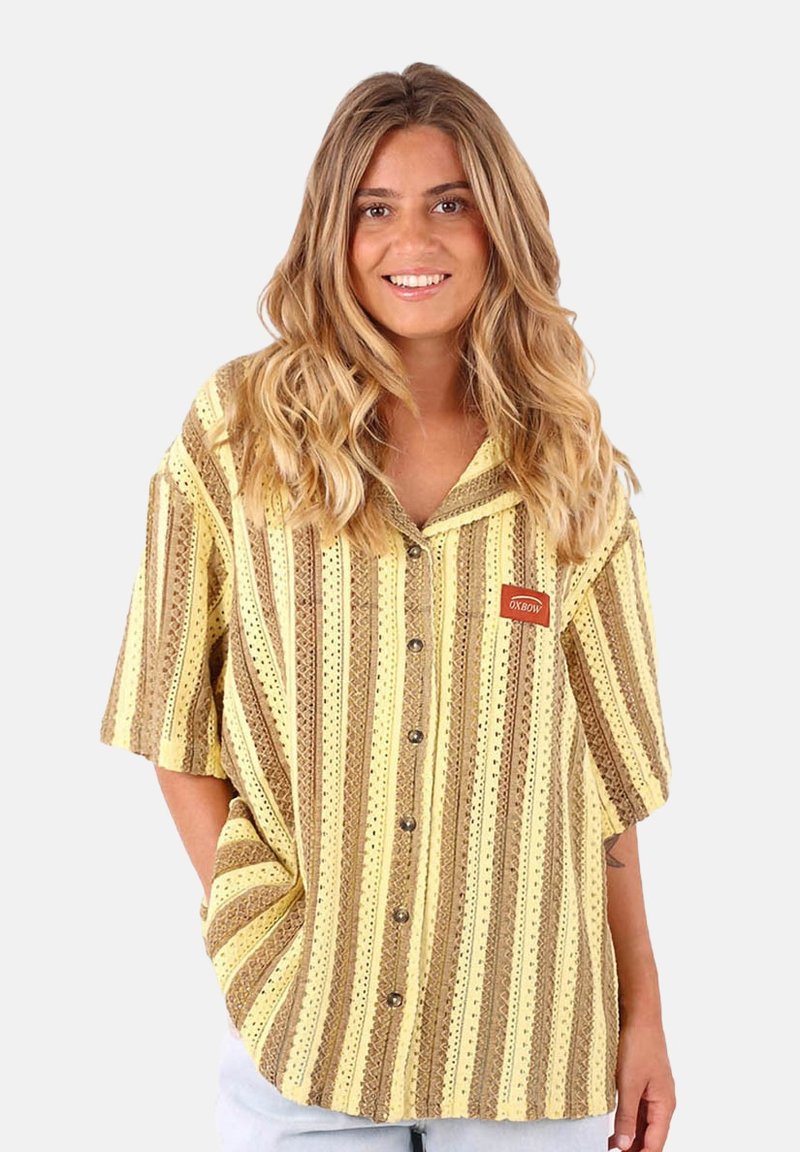 Chemise à manches courtes rayée jaune et marron avec un devant à boutons, présentant un petit logo brodé et un matériau texturé et respirant.