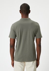 Oliven grønt kortærmet polo-shirt med krave. Blød, glat tekstur med en let tætsiddende facon. Synlige syninger ved kanten.