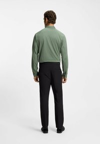 Camicia a maniche lunghe verde a fantasia, vista posteriore, abbinata a pantaloni neri su misura e scarpe nere. Tessuto liscio con un sottile design geometrico.