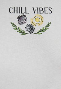 White cotton t-shirt featuring "CHILL VIBES" text, illustrated shells, a sun, and green leaf accents in a graphic design.