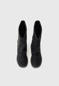 Zwarte suede enkellaarsjes met een slouchy ontwerp, ronde neus en platte rubberen zool. De bovenkant is gestructureerd en heeft een gladde afwerking.