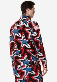 Giacca in fleece con un motivo a stelle multicolore in rosso, blu e nero. Presenta un logo "USA" bianco e una patch con la bandiera americana sulla manica.