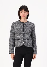 Grå og svart teksturert cardigan med rund halslinning, knappefront, to lommer og kontrasterende svart kant langs kantene.