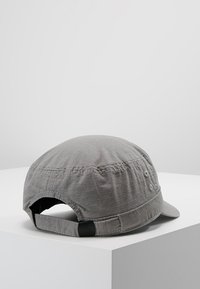 Gorra de algodón gris con una superficie texturizada, visera curva y correa ajustable en la parte posterior. Presenta sutiles detalles de costura.