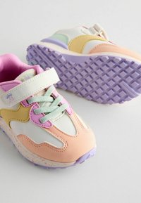 Baskets multicolores avec un mélange de matériaux roses, blancs, jaunes et verts, dotées d'une semelle lilas texturée et d'une sangle ajustable.