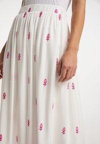 Fustă maxi albă cu broderie florală roz, talie elastică, material fluid și textură ușoară.