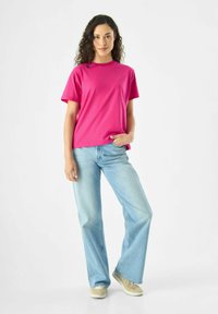 Korte mouwen roze t-shirt met een ronde hals, gecombineerd met lichtblauwe wijde jeans en beige sneakers, staande op een witte achtergrond.
