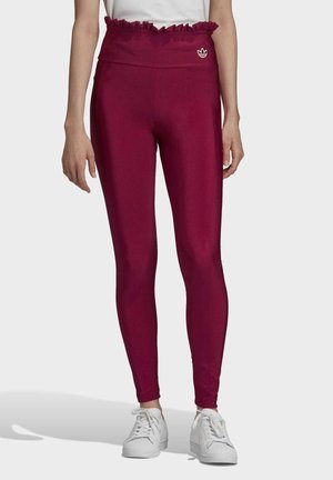 Vinröda leggings med en rynkad midjeresår, gjorda av mjukt, stretchigt tyg. Har en liten vit logga framtill, kombinerade med vita sneakers.