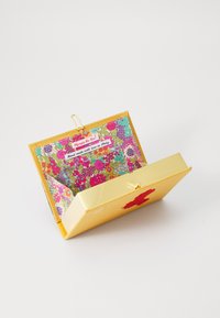 Boîte rectangulaire en or avec un intérieur à motif floral. Dispose d'un rabat plié et d'un accent rouge. Comprend une étiquette indiquant "Fait à la main avec amour en Italie."