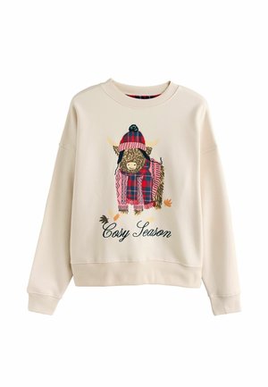 Krämfärgad sweatshirt med en central grafik av en höglandsko som bär en randig scarf och hatt. Texten säger "Mysig Säsong" i grönt.