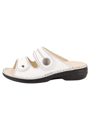 Biała sandałka z odkrytymi palcami, z dwoma regulowanymi paskami ozdobionymi okrągłymi metalowymi guzikami oraz czarną, amortyzowaną podeszwą.