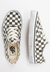 Baskets en toile à damier noir et crème avec des lacets blancs, semelle en caoutchouc et logo Vans sur la semelle intérieure. La vue de côté montre la tige texturée.