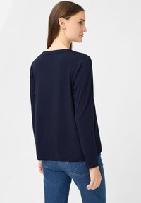 Maglione a maniche lunghe navy realizzato in un tessuto morbido, con scollatura rotonda e vestibilità rilassata, abbinato a jeans azzurri chiari.