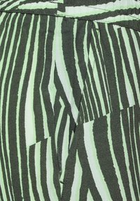 Texturerad tyg i grönt och svart, med ett zigzag-mönster med varierande randbredder och en synlig sömdetalj.