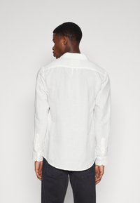 Camicia bianca in lino a maniche lunghe con colletto, polsini con bottone e orlo curvo. Tessuto pulito e testurizzato con una vestibilità rilassata.