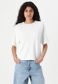 Top corto bianco a maniche corte con scollatura rotonda e maniche raglan, realizzato in tessuto testurizzato, abbinato a jeans a vita alta blu chiaro.