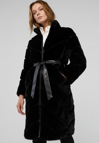 Cappotto in pelliccia sintetica nera con motivo a zigzag, collo alto, chiusura con zip e cintura in satin removibile. Maniche lunghe, texture morbida e finitura liscia.