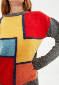 Bunter Strickpullover mit Blockmustern in Rot, Gelb, Blau und Grau, mit einem gerippten Halsausschnitt und Bündchen, die unterschiedliche Texturen betonen.