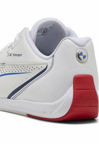 Bílé sportovní boty s modrými akcenty, perforovaným bočním designem a červeným podpatkem. Mají hladký povrch a zadní logickou emblému.
