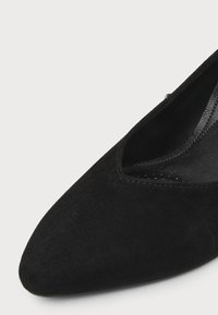 Gros plan sur l'avant et le côté d'une chaussure noire en daim à bout pointu avec coutures visibles et semelle intérieure lisse.