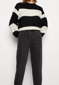 Svartvit randig stickad tröja med rundad halsringning, kombinerad med högmidjade svarta jeans i denim med knäppning.