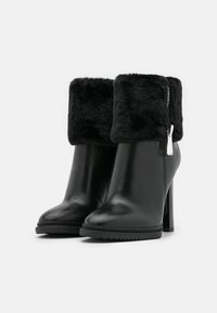 Černé kožené kotníkové boty s umělou kožešinou na lemu. Mají vysoký podpatek, hladký povrch a boční zip pro zavírání.