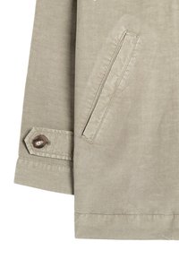 Lys beige jakke med lynlås foran, sidelomme og knapdetalje ved ærmet. Glat tekstur med et afslappet design og moderne finish.